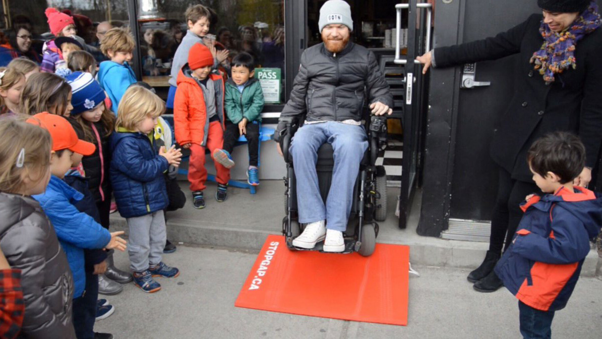 luke anderson drives his wheelchair down a stopgap ramp while children look on
