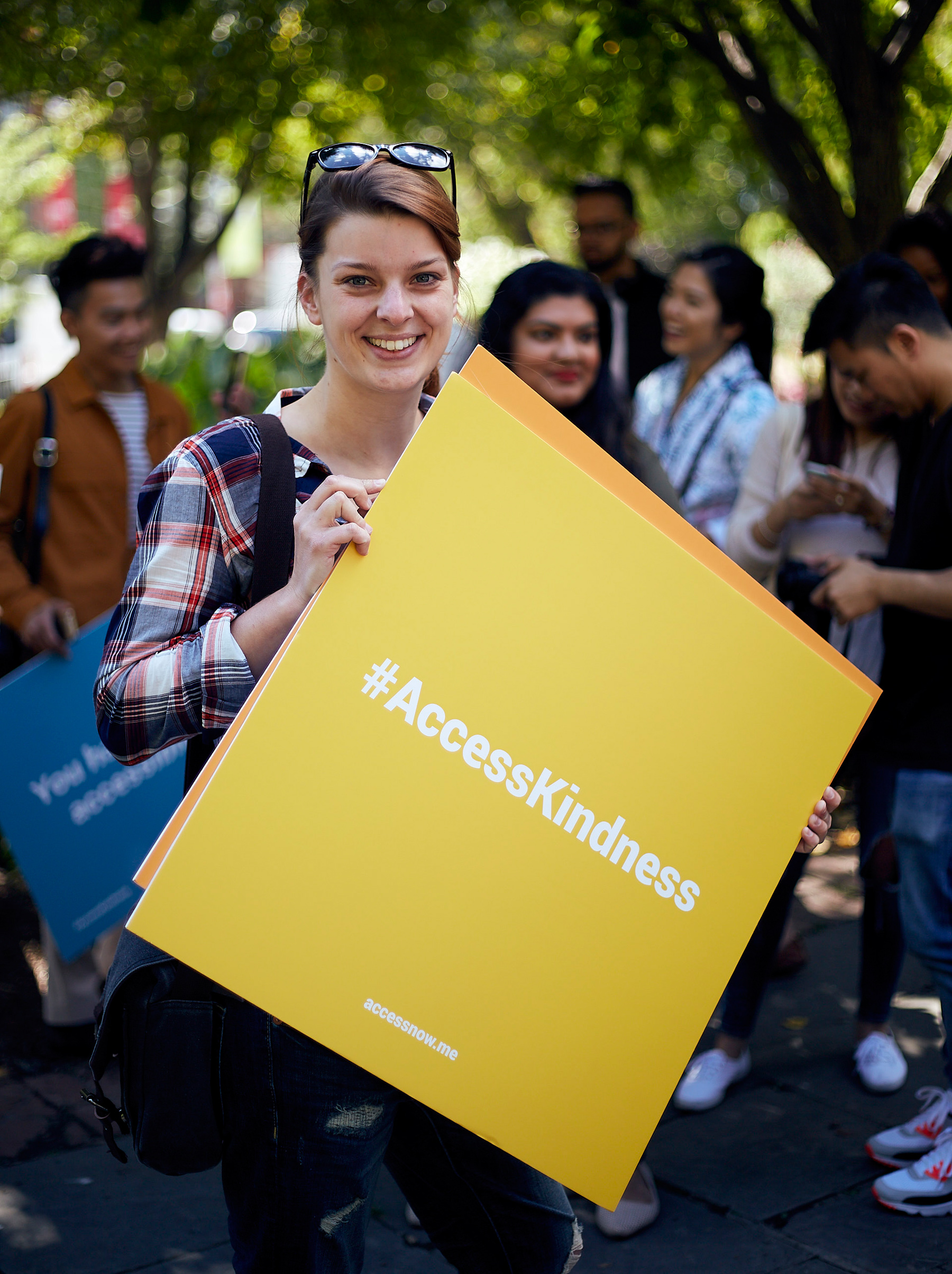 photo of young woman smiling as she holds up a yellow sign that reads "Access Kindness" in bold 