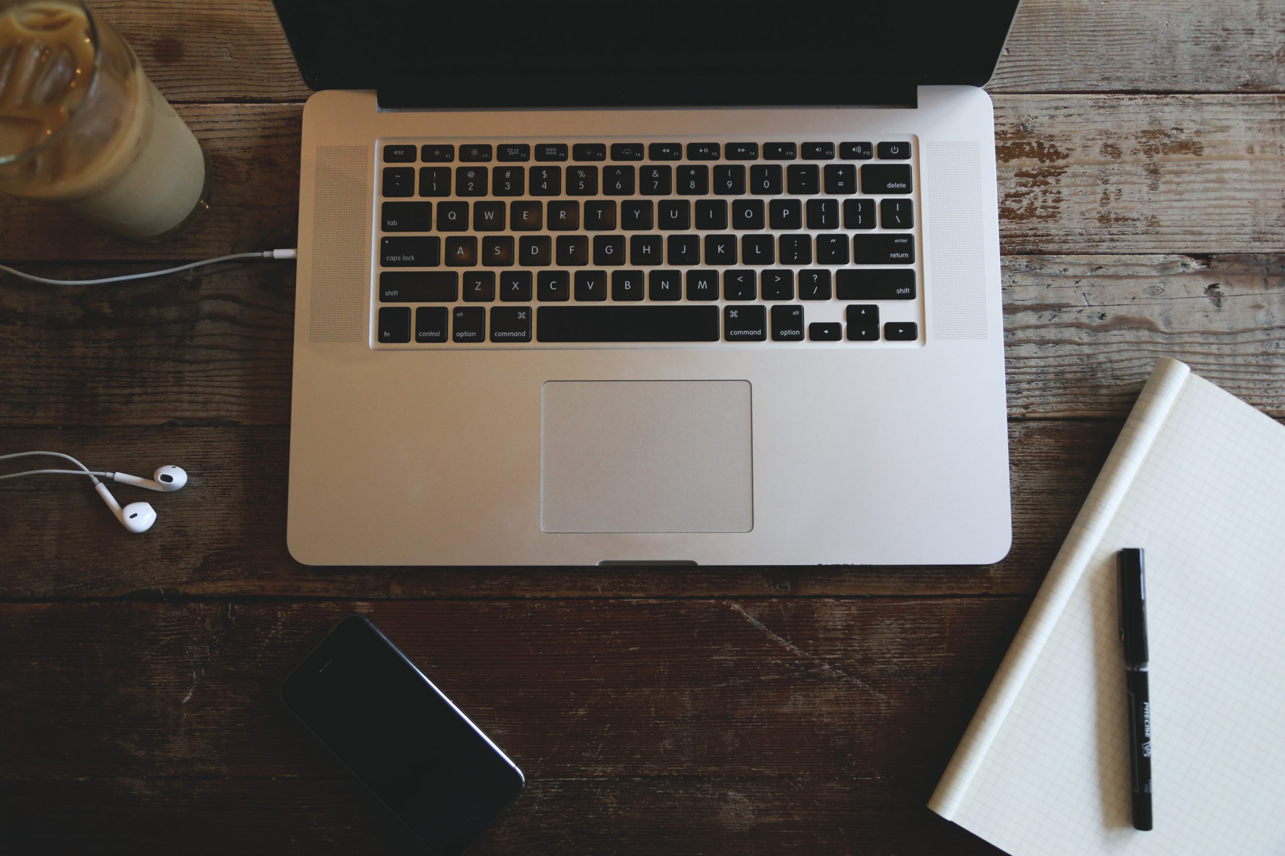 Photo of an organized desk with a laptop, earphones, notebook and pen