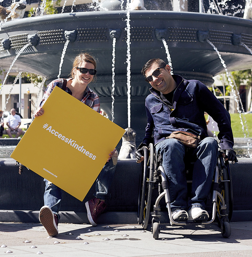 deux personnes sourient, l'une en fauteuil roulant, l'autre non.