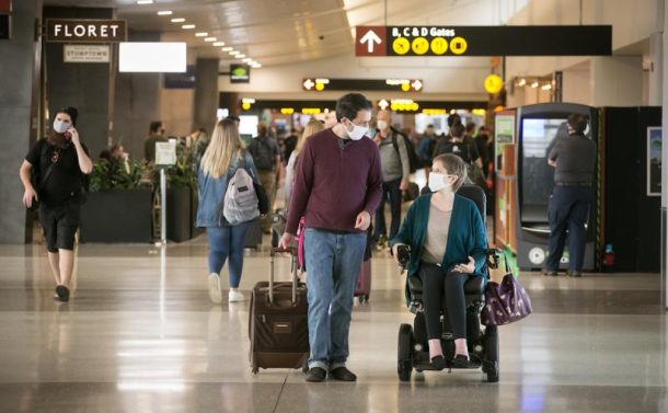 a woman using a power wheelchair and able-bodied man walk through an airport