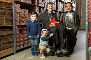 billy price in his wheelchair smiles with 3 kids in the shoe warehouse