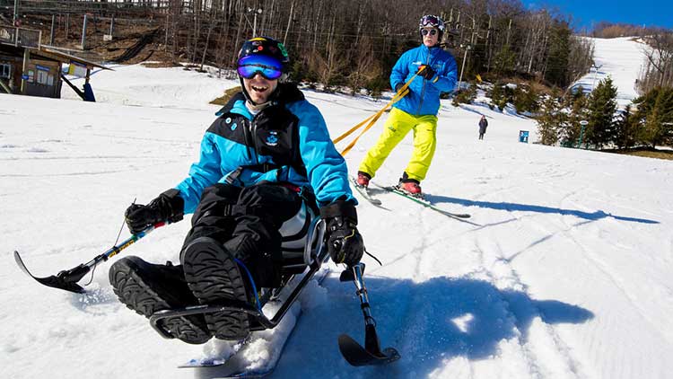 man sits in a adaptive sitski on a snowy hill