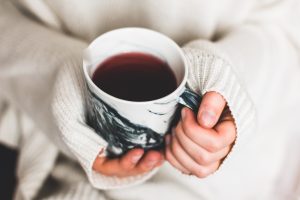 closeup shot of hands in cozy sweater sleeves holding a mug of hot tea