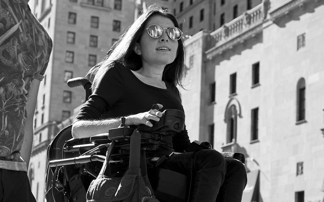black and white photo of maayan ziv driving her wheelchair on a busy sidewalk.