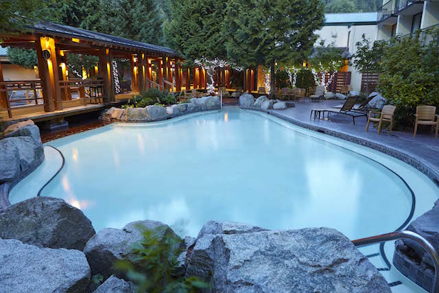 A large, empty pool at Harrison Hot Springs resort. The pool is surrounded by beautiful large rocks and on the left side, there is a covered over wooden pathway that leads to other pools.