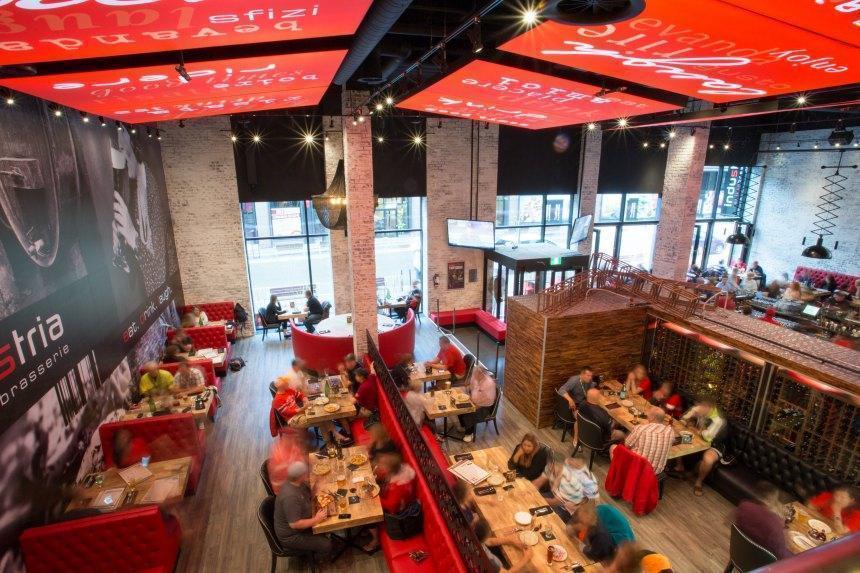 Interior of Industria Pizzeria Bar. High ceilings and red accents in the space including the chairs. Several booth style but also low-top tables. 