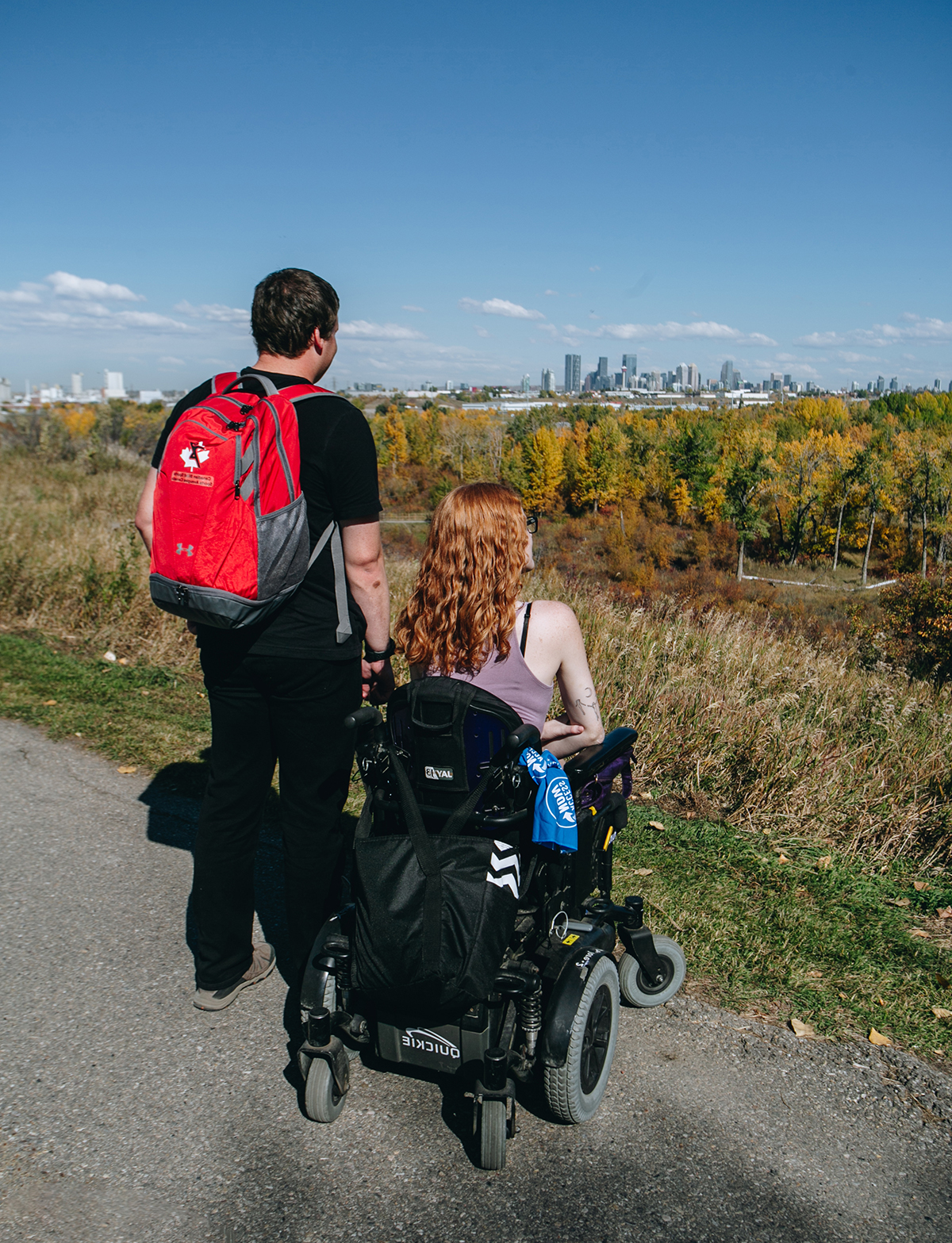 deux personnes regardent un parc de la ville de calgary. par une journée ensoleillée. une personne est assise sur un fauteuil roulant électrique.