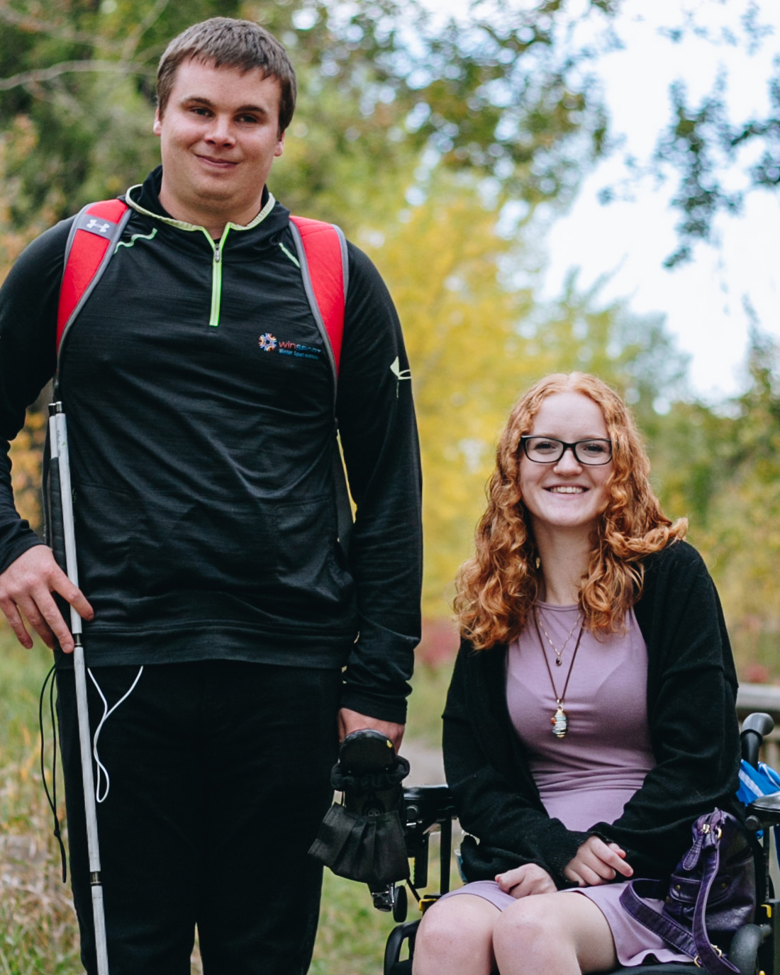 Aaron, à gauche, sourit en tenant sa canne, et Alex, à droite, sourit dans son fauteuil roulant.