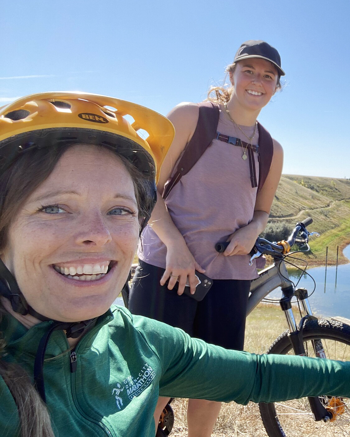 deux femmes caucasiennes souriant au soleil, l'une sur un vélo, l'autre sur un vélo à main