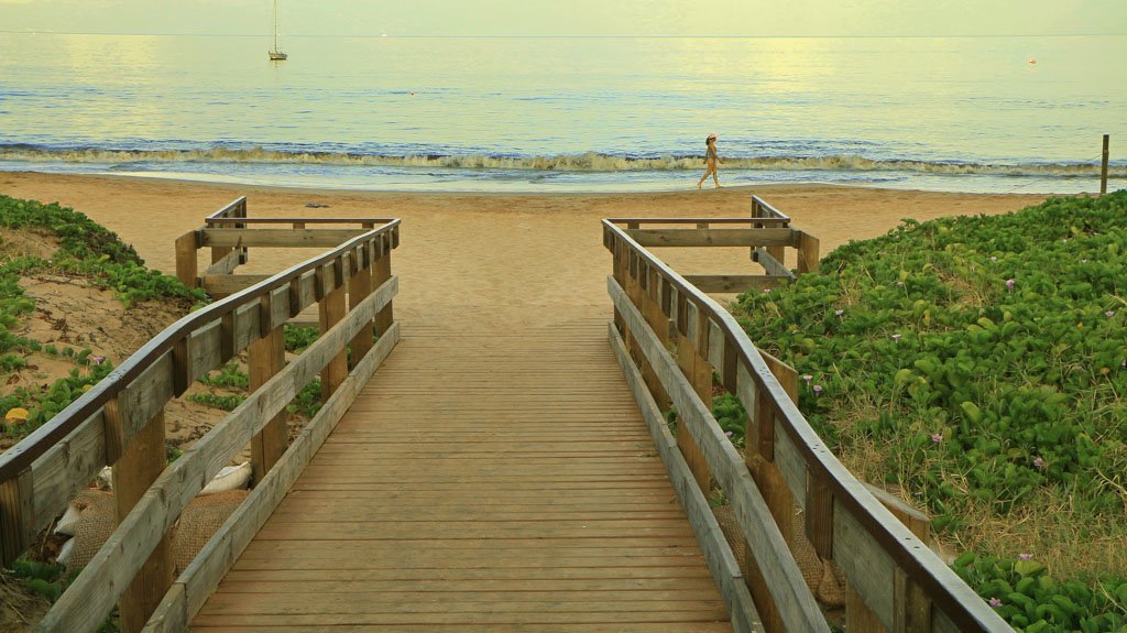 A long wooden boardwalk that leads to the sand at Kama’ole I Beach Park. 
