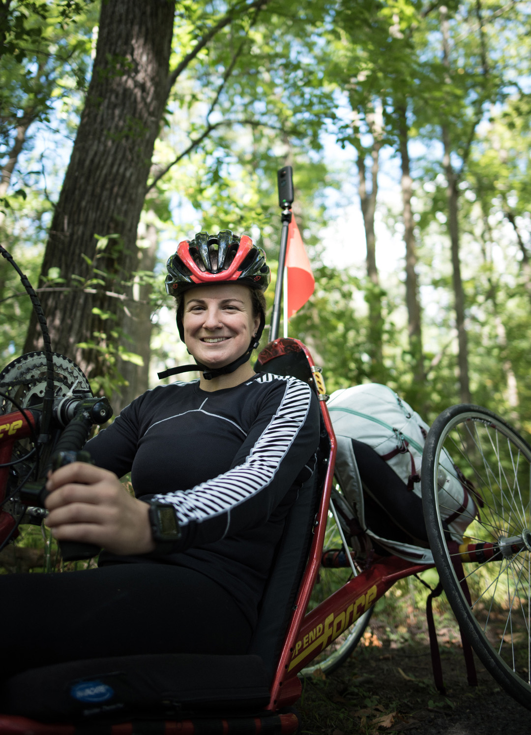 camille is smiling as she sits in her hand cycle in a wooded area 