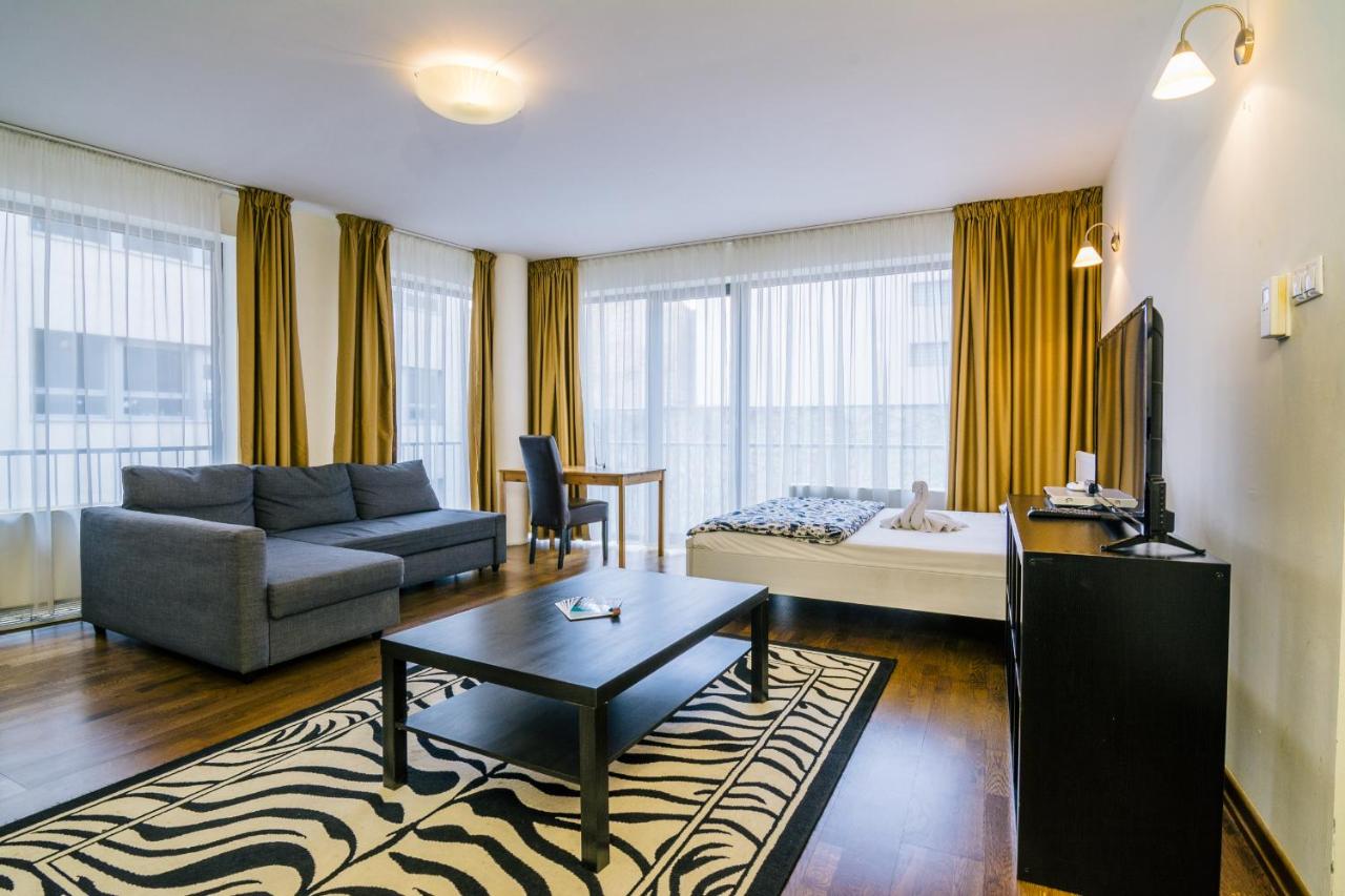 bedroom at luxury downtown apartments. there is a bed, a coffee table, a couch, a small cabinet and a tv is on top, rug with black and white pattern, windows are big with a lot of natural lighting
