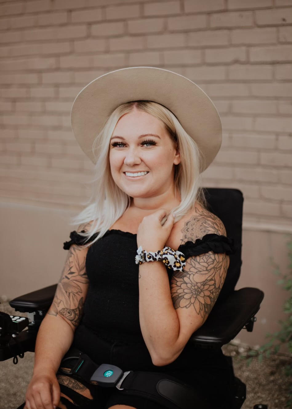 Bio photo of Shailynn Taylor. She is sitting on her wheelchair, has several arm tattoos and wearing a wide brim hat.