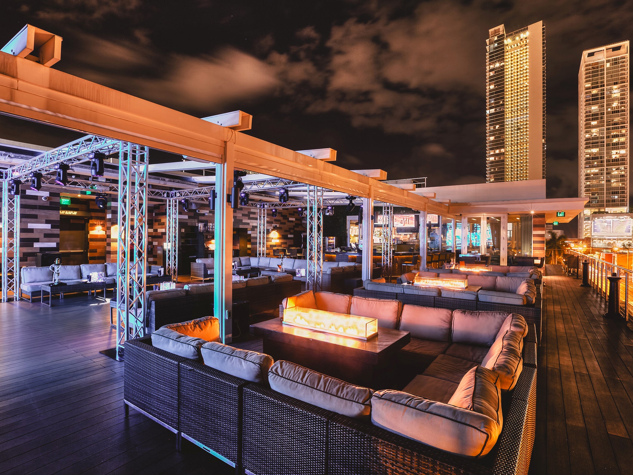 Rooftop at night with neon lights and lowered couches with high rise buildings in the background