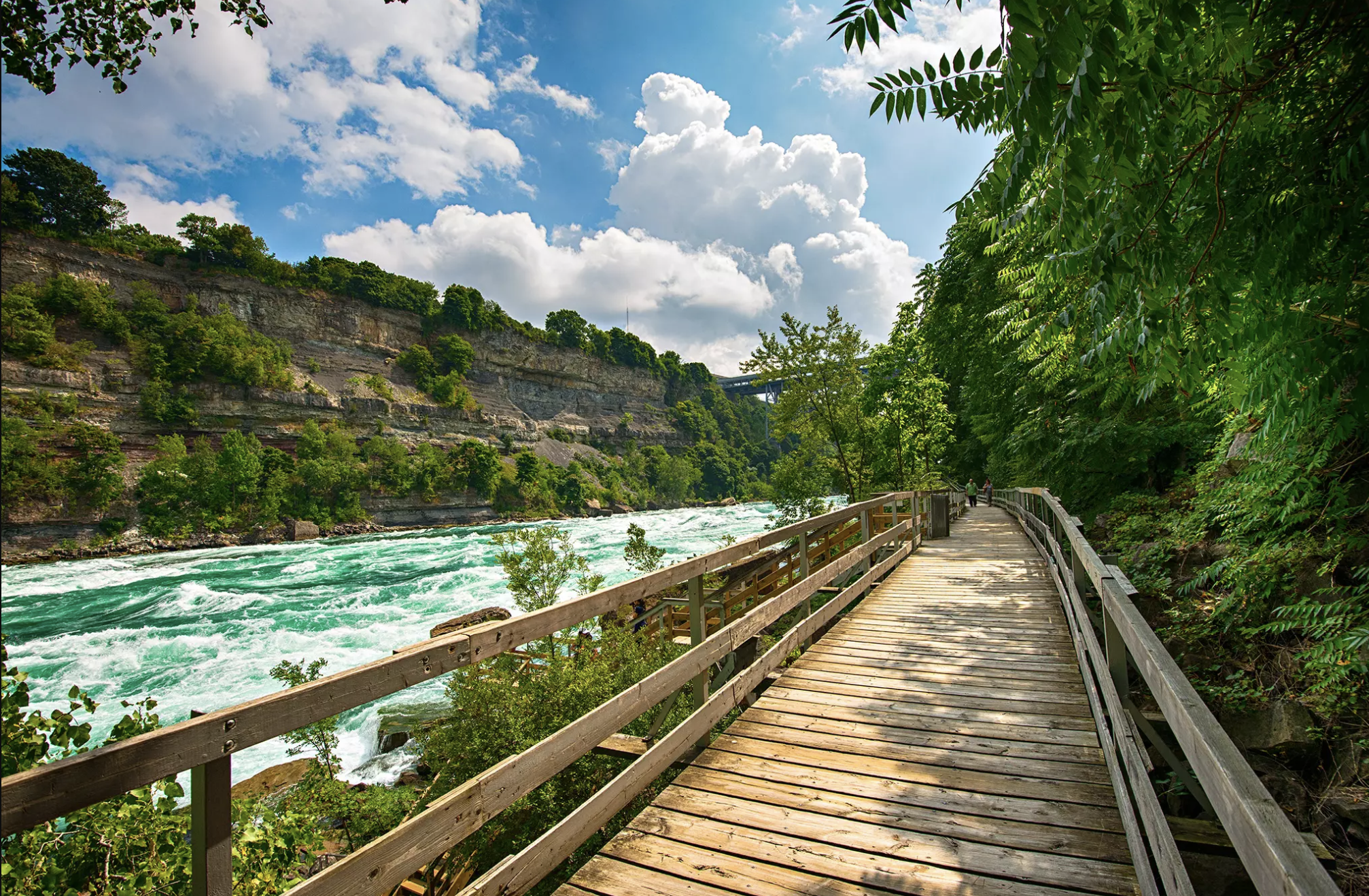 nice wooden bridge by the lake. beautiful backdrop of blue skies, clouds, mountains and lush green trees 