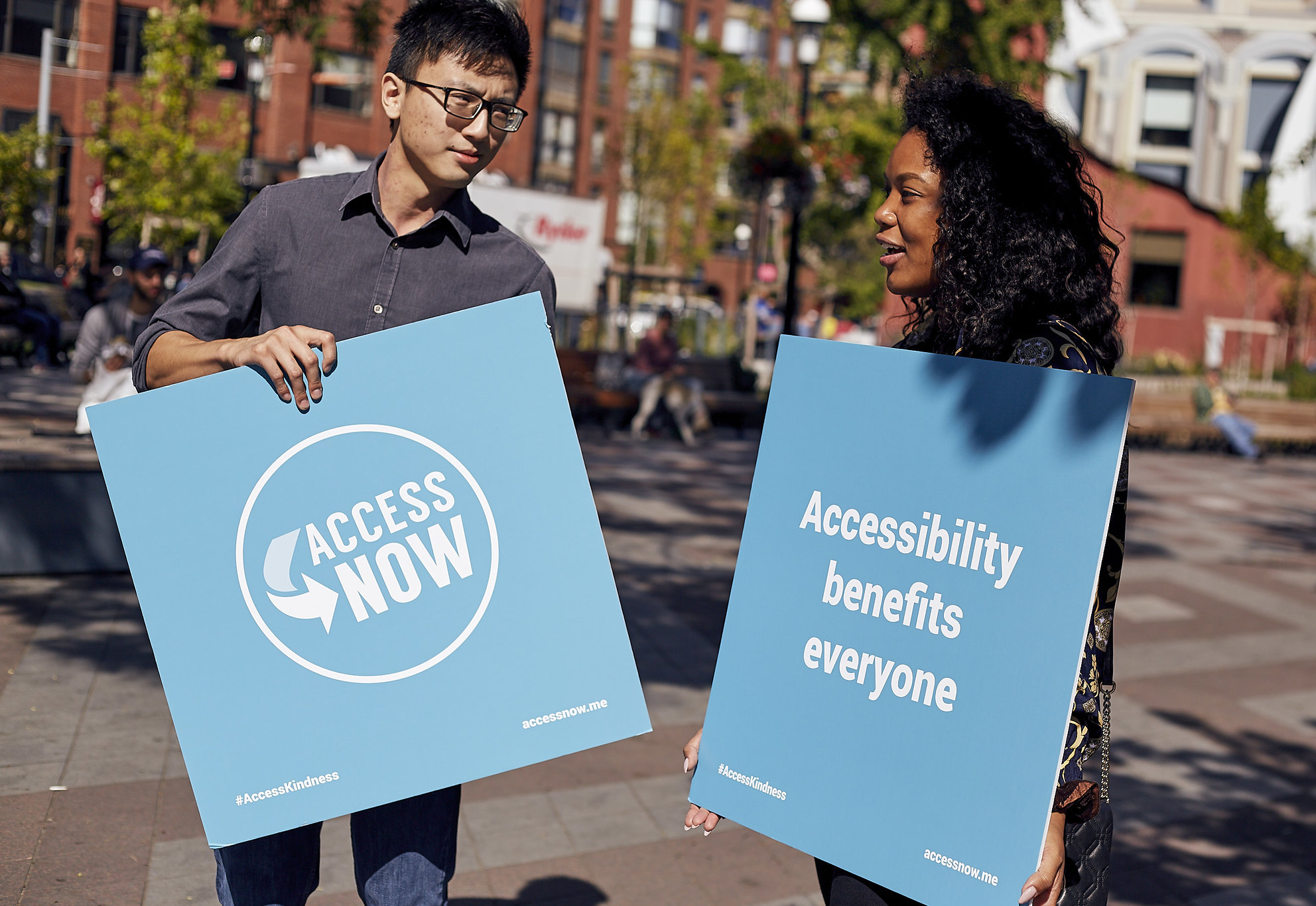 an asian man and black woman hold signs with accessnow logos on them