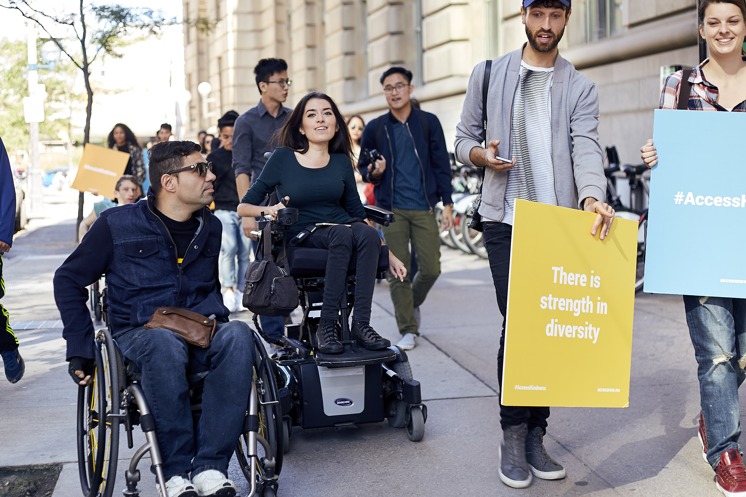 a group of interabled people walk down a city sidewalk, some hold signs that say "you had me at accessible"