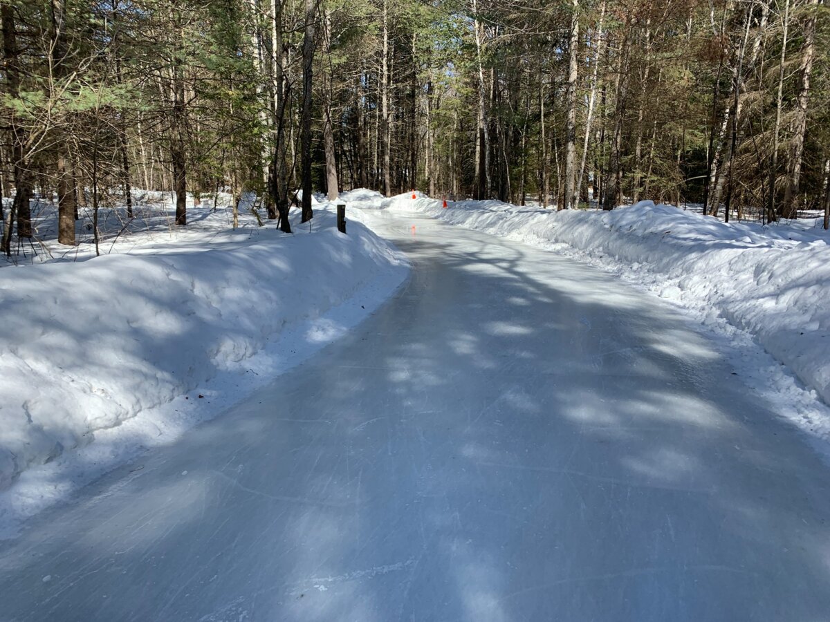 daytime image of a trail that is entirely ice in the midst of the woods