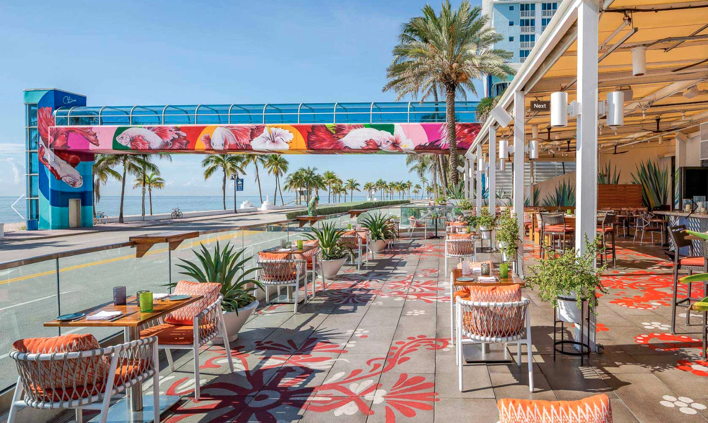 colourful exterior of lona restaurant with ocean front views and palm trees.
