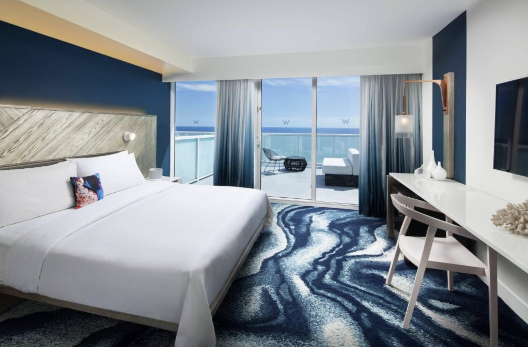blue toned hotel room with king bed and walk out balcony overlooking the ocean