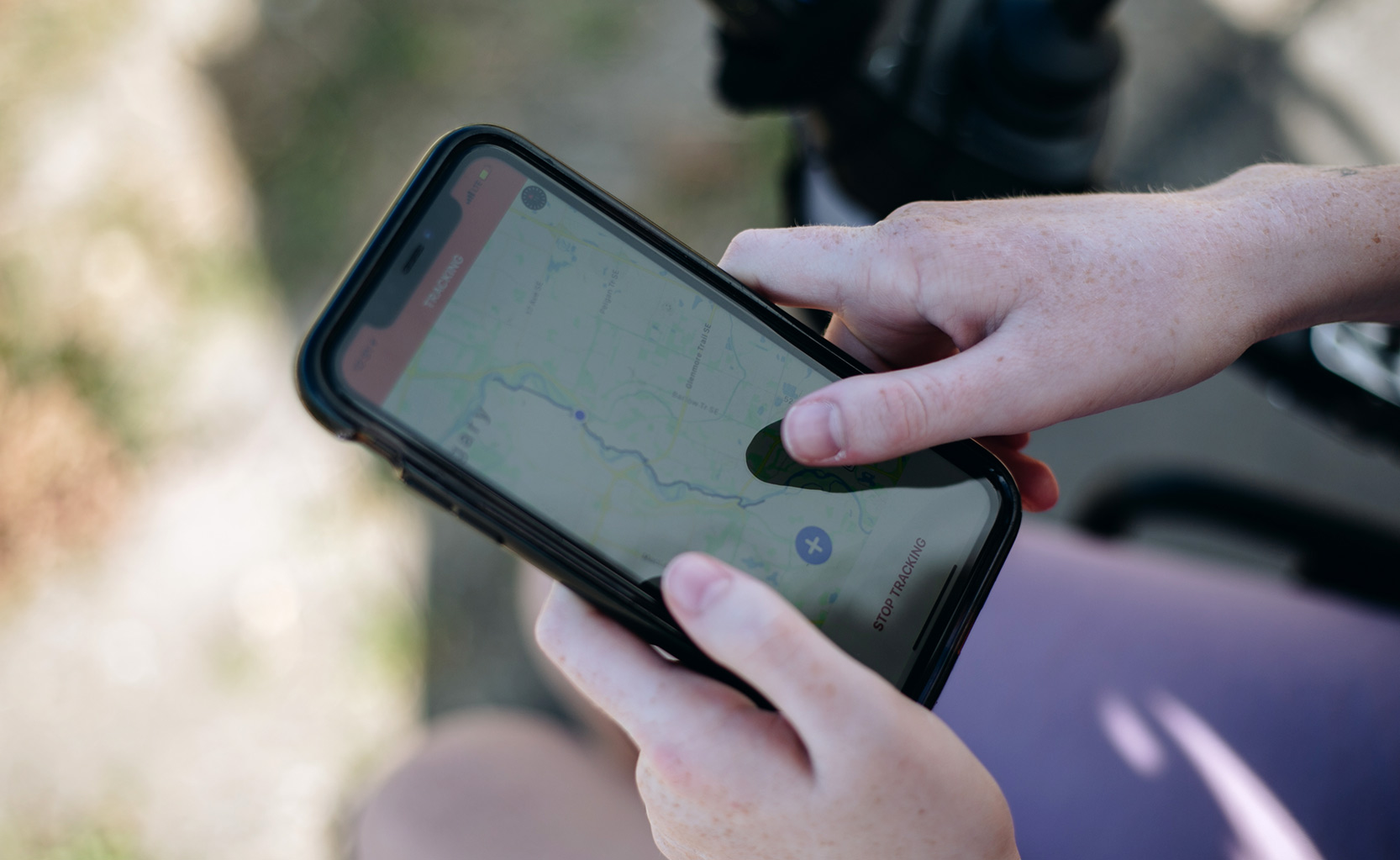 Image d'une femme assise dans son fauteuil roulant montrant l'écran de son téléphone avec un accès à une carte extérieure montrant une ligne de sentier bleue.