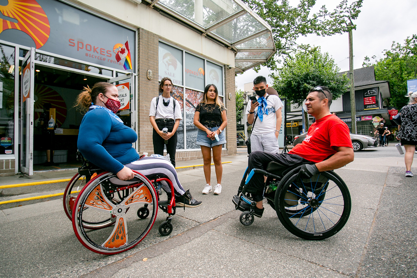 inter-abled gathering of 5 people on a vancouver sidewalk. two are wheelchair users
