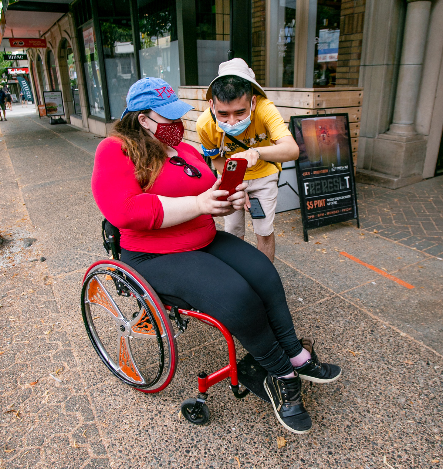 a wheelchair user and a standing person look at a phone together
