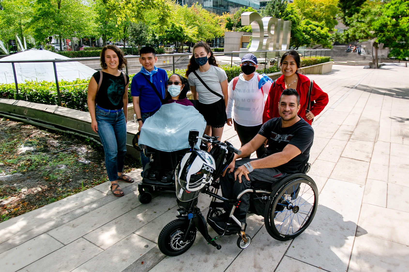 two wheelchair users and a few standing people pose in a green courtyard outside UBC