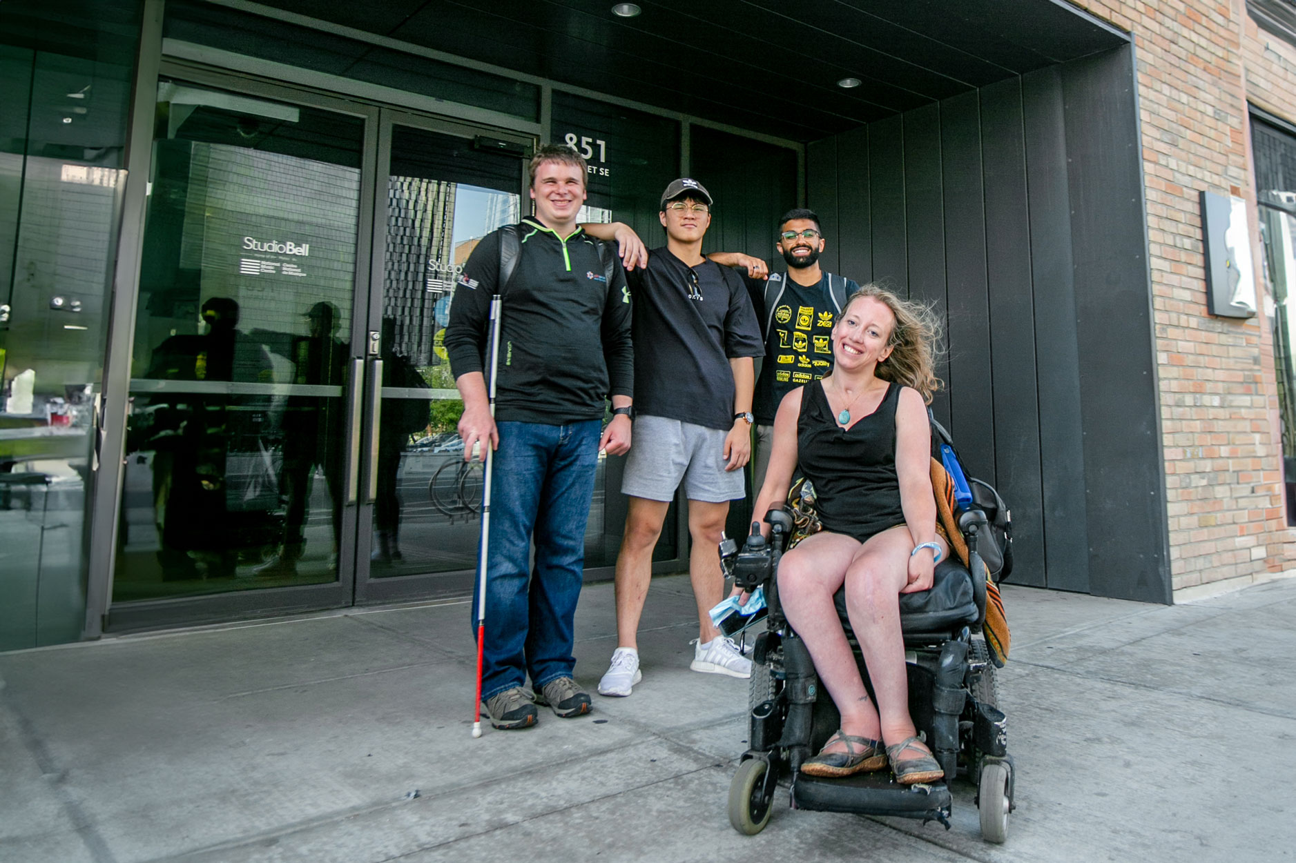 MOCA-2021-YYC---Photo-by-Alexa-Fernando---19 jocelyn who sits in a power wheelchair smiles posing with aarron who holds his white cane, alex, and one more person.