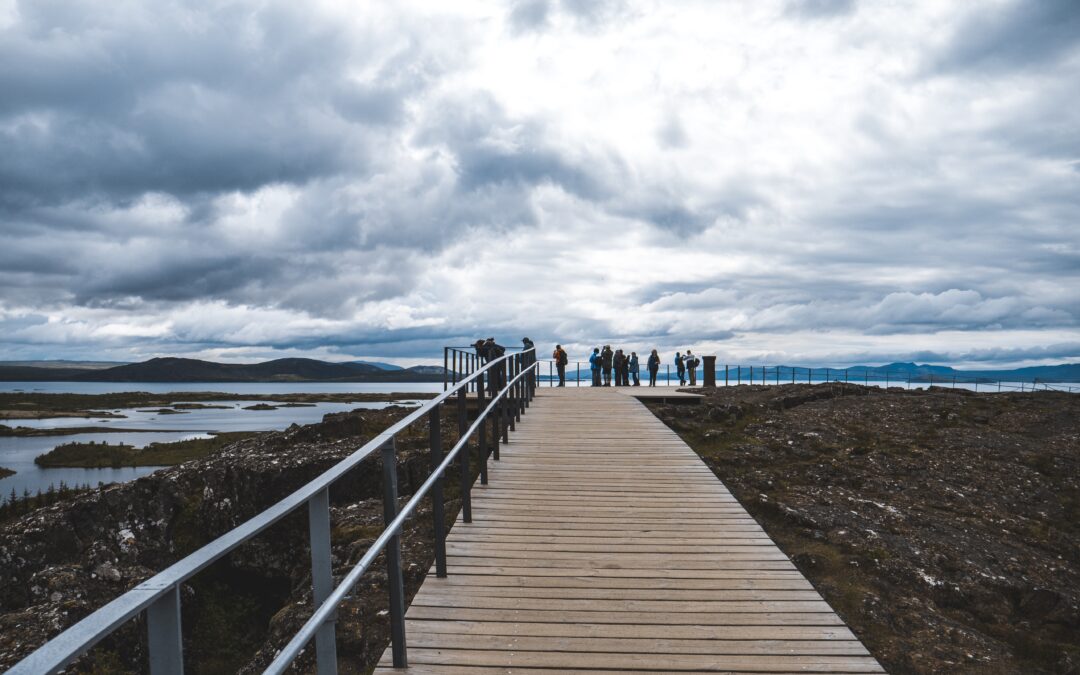 A long shot of a boardwalk with railing and tourists, overlooking a lake on a cloudy day