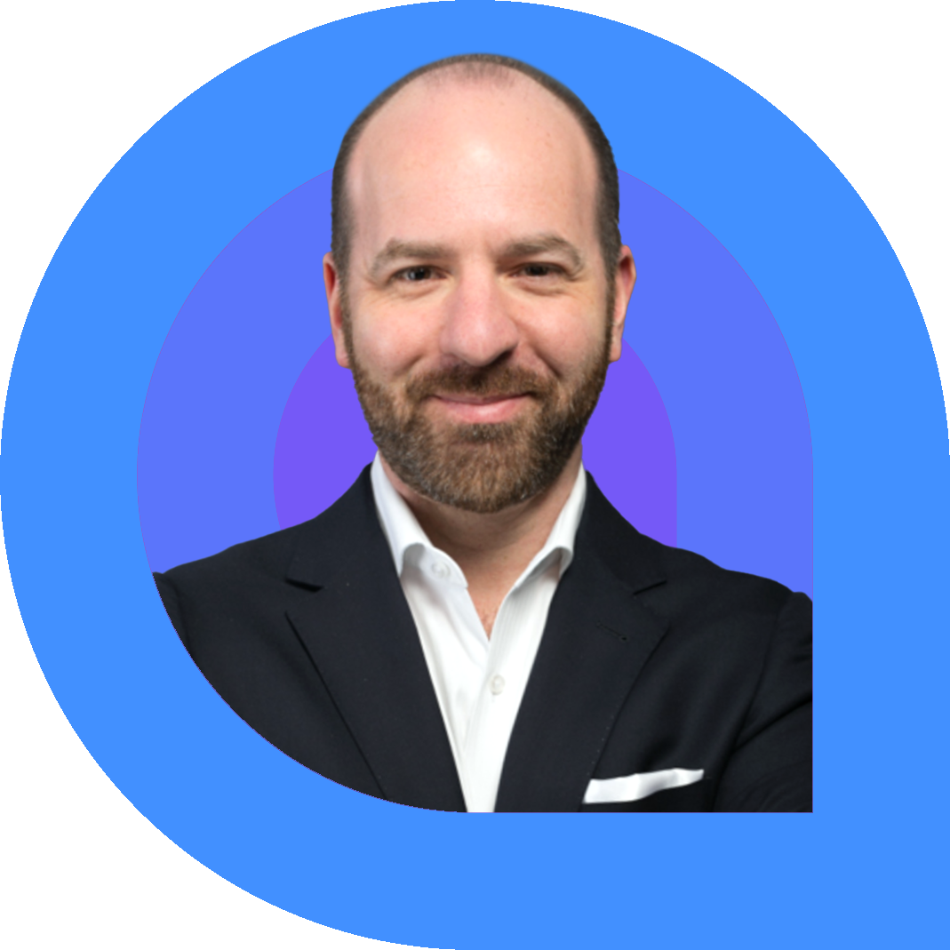 Andrew, a man with a trimmed beard and shaved head, smiles confidently while wearing a black suit jacket, white dress shirt, and pocket square.