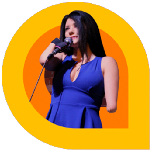 Courtney Gilmour, a comedian with long dark hair, stands on stage holding a microphone. She wears a sleeveless royal blue dress and smiles while performing. The image is framed within a bold yellow graphic shape, creating a vibrant and energetic look.