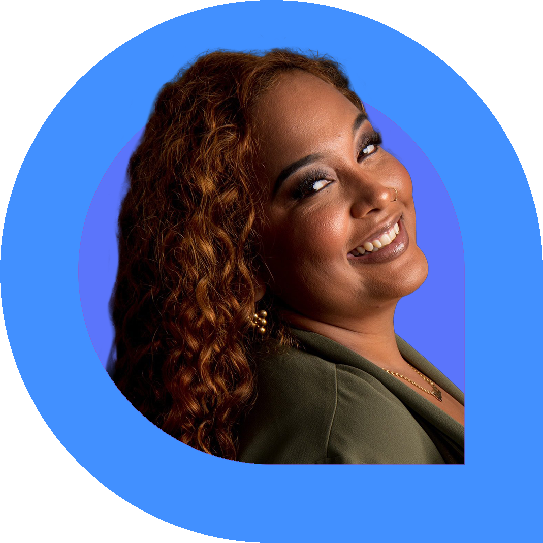 Portrait of Gaitrie smiling woman with long curly auburn hair, wearing a green blazer and gold earrings, posed against a bright blue and purple background framed in a bold pink and blue graphic shape