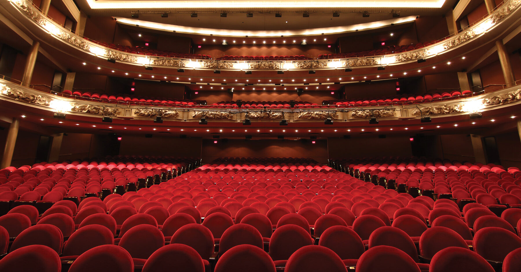 interior of grand princess of wales theatre. red seating and gold lighting.