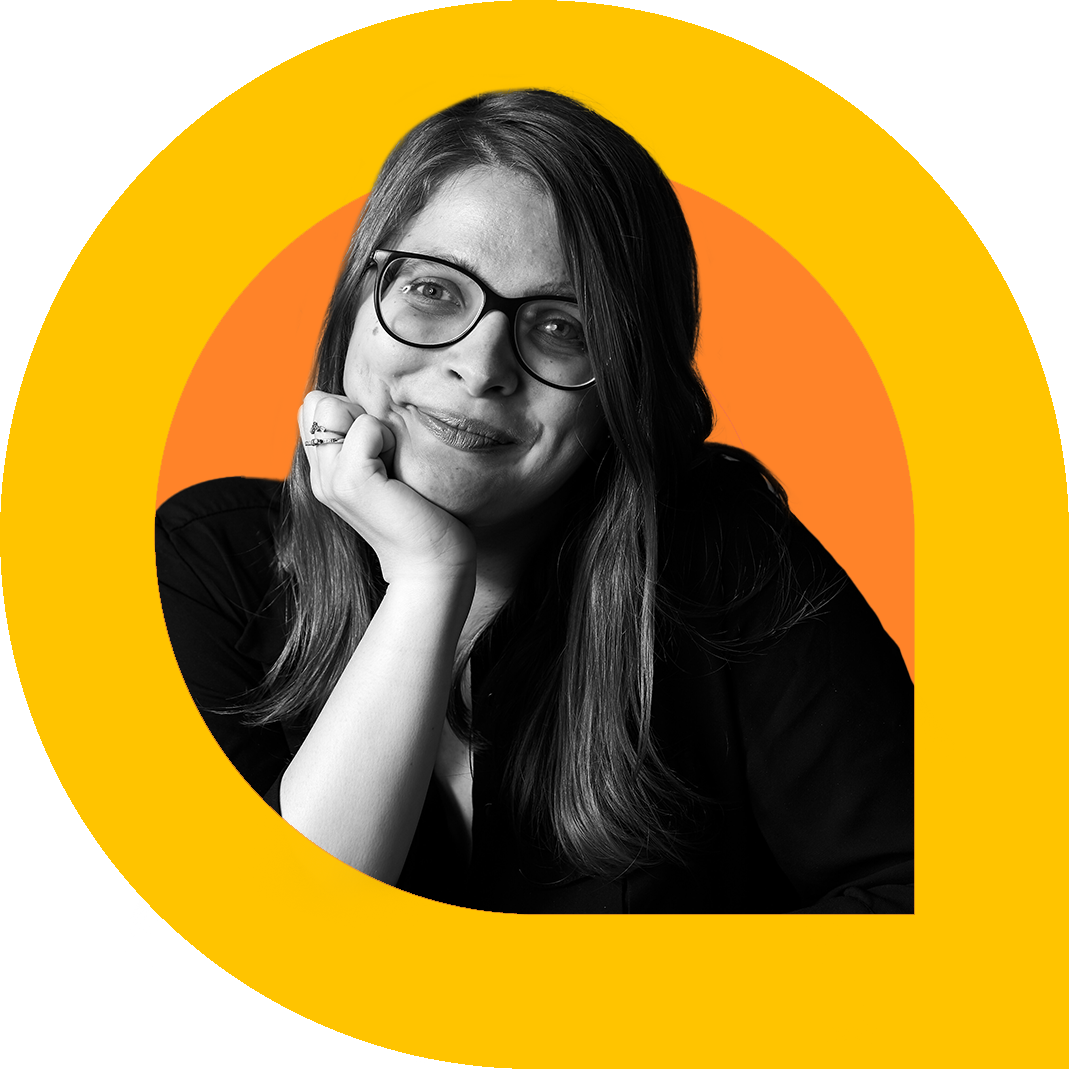 A black and white portrait of Jess, a woman with long hair and glasses, smiling gently with her chin resting on her hand. She wears a dark top and rings on her fingers.