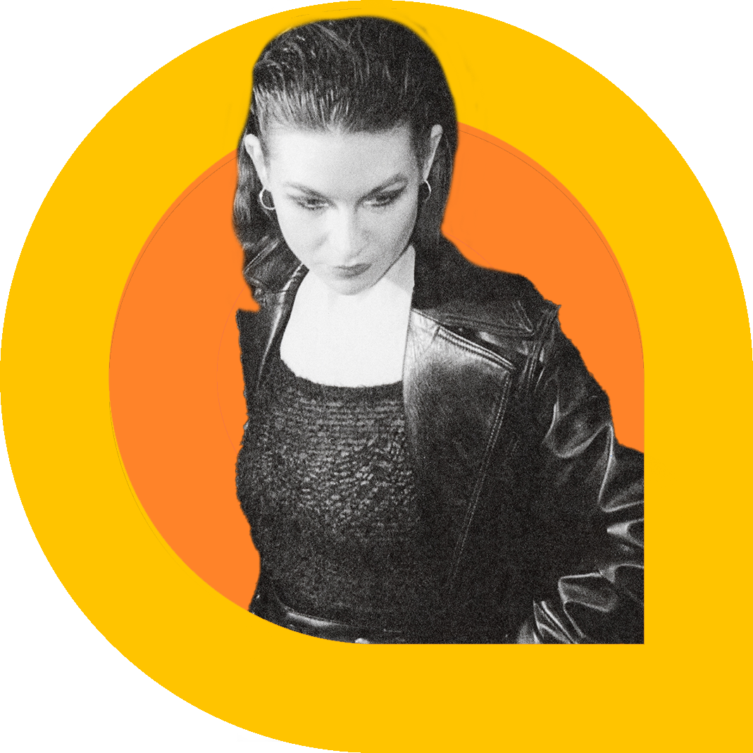 A black and white portrait of Stefana Fratila, looking down with a contemplative expression. She wears a textured top and a leather jacket, framed by bold graphic rings in pink, yellow, and orange that create a dynamic, modern backdrop.