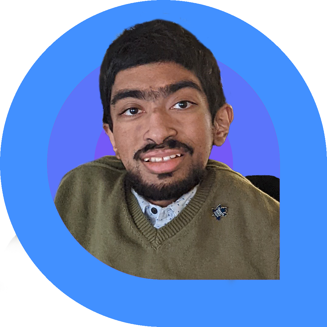 Portrait of a smiling young man with short dark hair and a trimmed beard, wearing a green sweater with a pin and a collared shirt, against a bold blue and purple circular background framed in pink