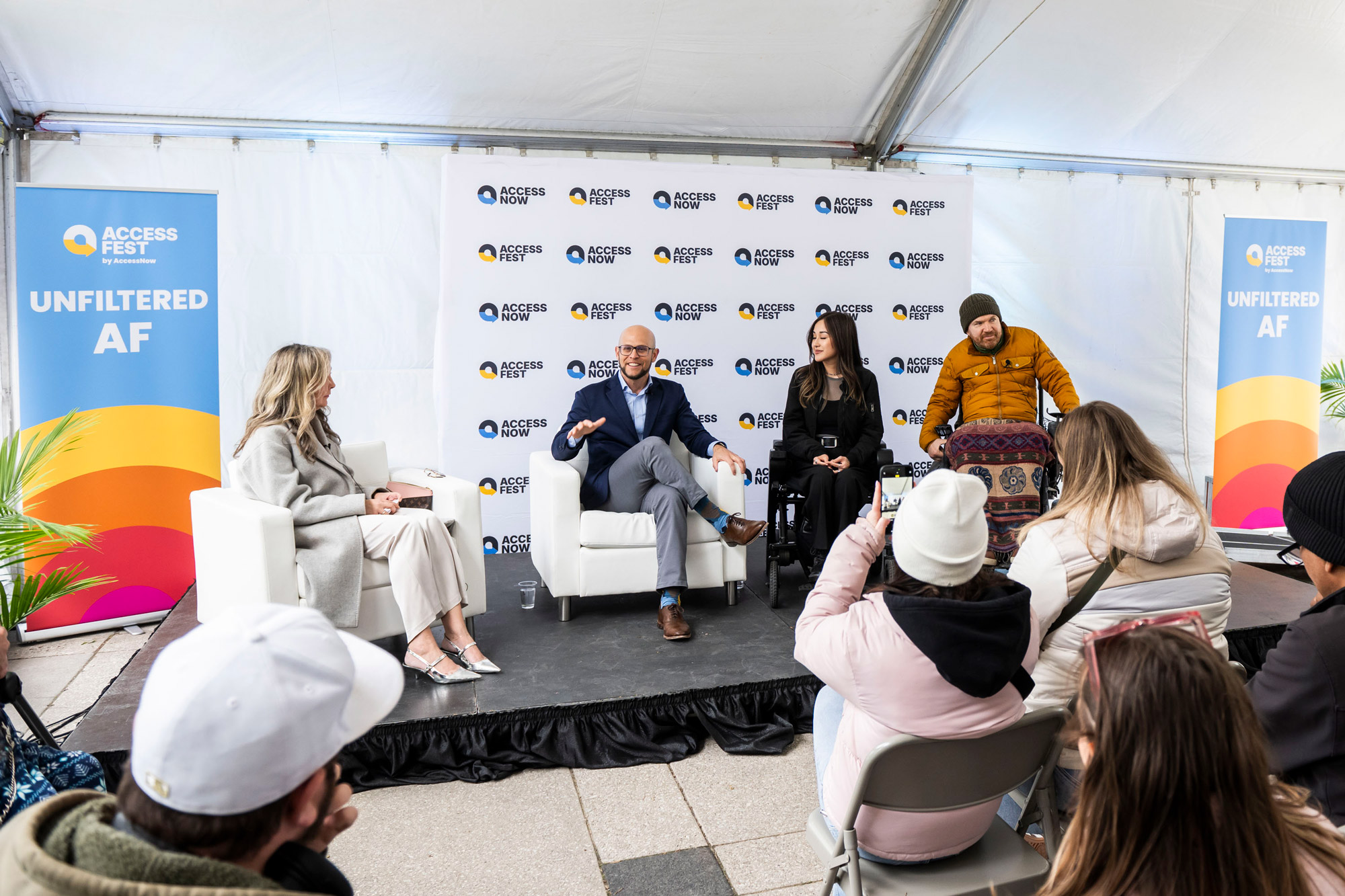 Three people participate in a fireside chat panel on stage. Two panelists using power wheelchairs sit in front of banners that read 'AccessNow' and 'The Future is Smart, Built for Everyone.'