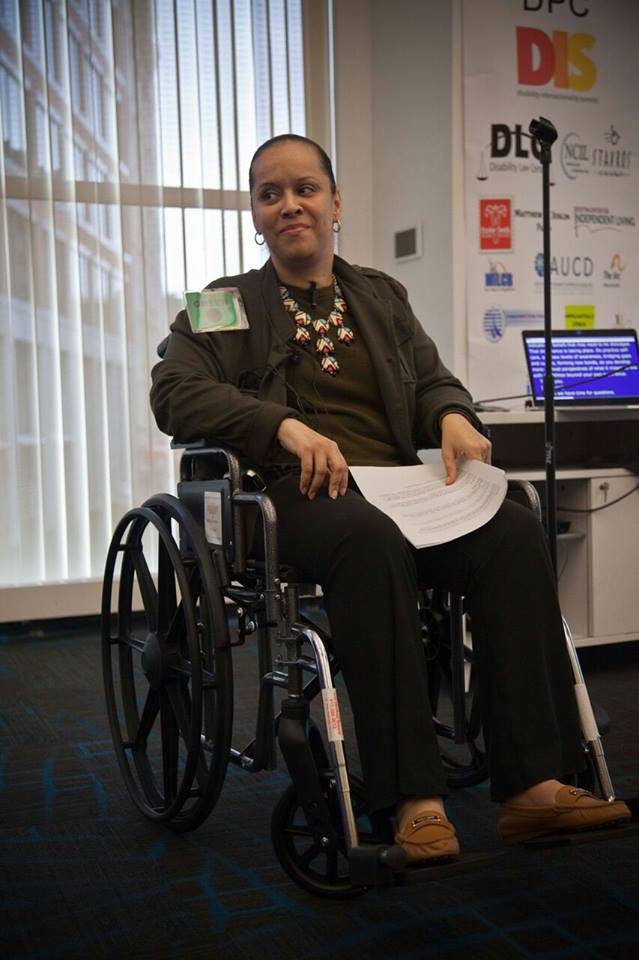 Heather watkins smiling in her wheelchair, holding a piece of paper