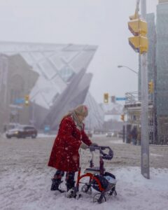 Senior woman in Toronto using walker for moving alone through snowy, inaccessible pathway.