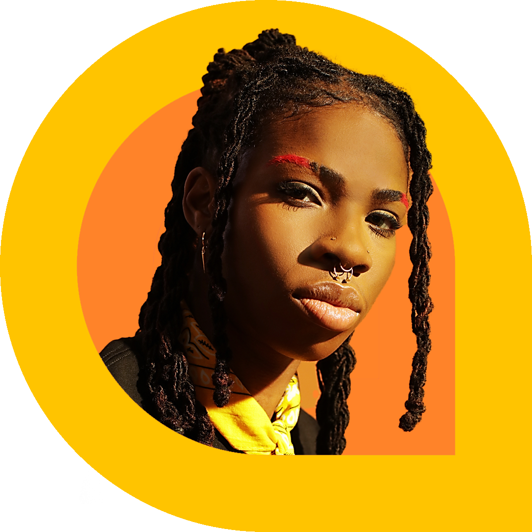 Close-up portrait of haviah mighty with long locs, a septum piercing, and bold red eyebrow accents, looking toward the camera against a warm orange background.
