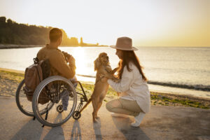 An interabled couple travelling with a dog, enjoying the sunset on a beach.
