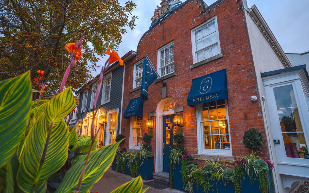Red brick exterior of 124 on Queen Hotel and Spa at dusk, with blue awnings, warm window lights and flowering planters out front.